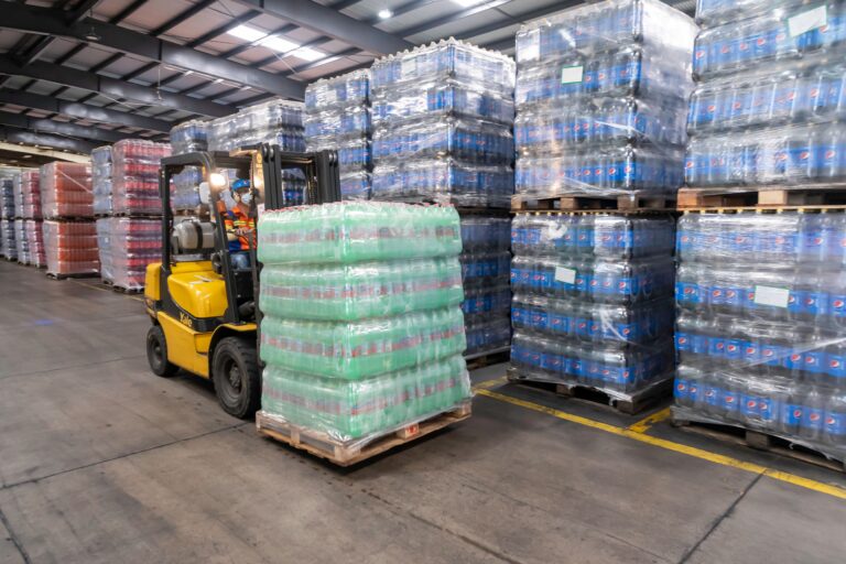 Forklift operator moving stacked pallets in a busy warehouse, a site where a warehouse ANPR system controls vehicle entry
