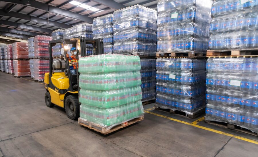 Forklift operator moving stacked pallets in a busy warehouse, a site where a warehouse ANPR system controls vehicle entry