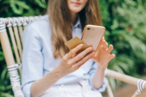 Wanita memakai smartphone dan kartu, ilustrasi liveness detection e-KYC pada aplikasi fintech
