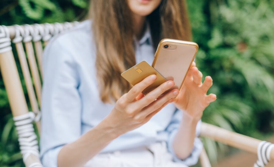 Wanita memakai smartphone dan kartu, ilustrasi liveness detection e-KYC pada aplikasi fintech